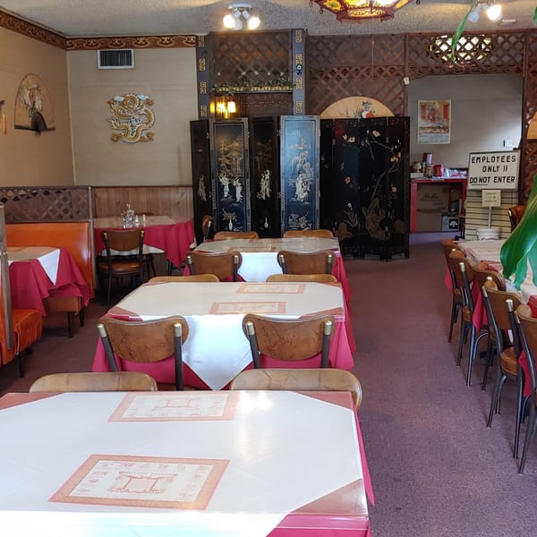 Empty Chinese restaurant dining room with red tablecloths, orange booths, and decorative screens.