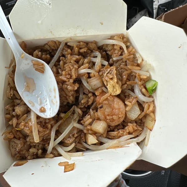 Shrimp fried rice with bean sprouts and onions in a white takeout box with a plastic spoon.