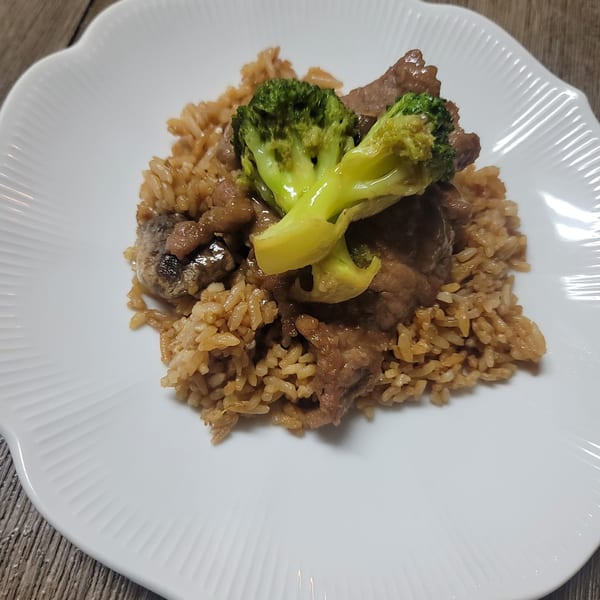 Beef and broccoli stir-fry with brown rice, served on a white scalloped plate.