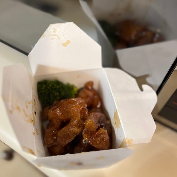 Two open takeout containers filled with orange chicken and broccoli, with one in focus.