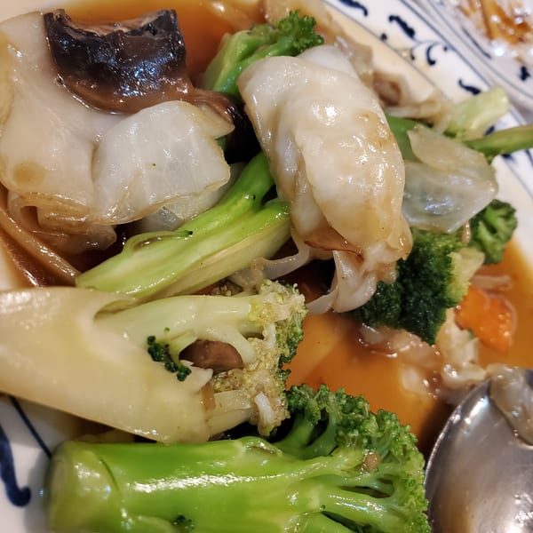 Stir-fried broccoli, bok choy, and mushrooms in a savory brown sauce on a white and blue plate.