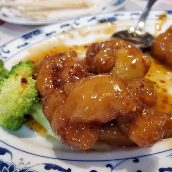 Sweet and sour chicken with broccoli florets on a white and blue patterned plate.