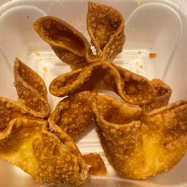 Several golden-brown, crispy crab rangoon appetizers are served in a white takeout container.