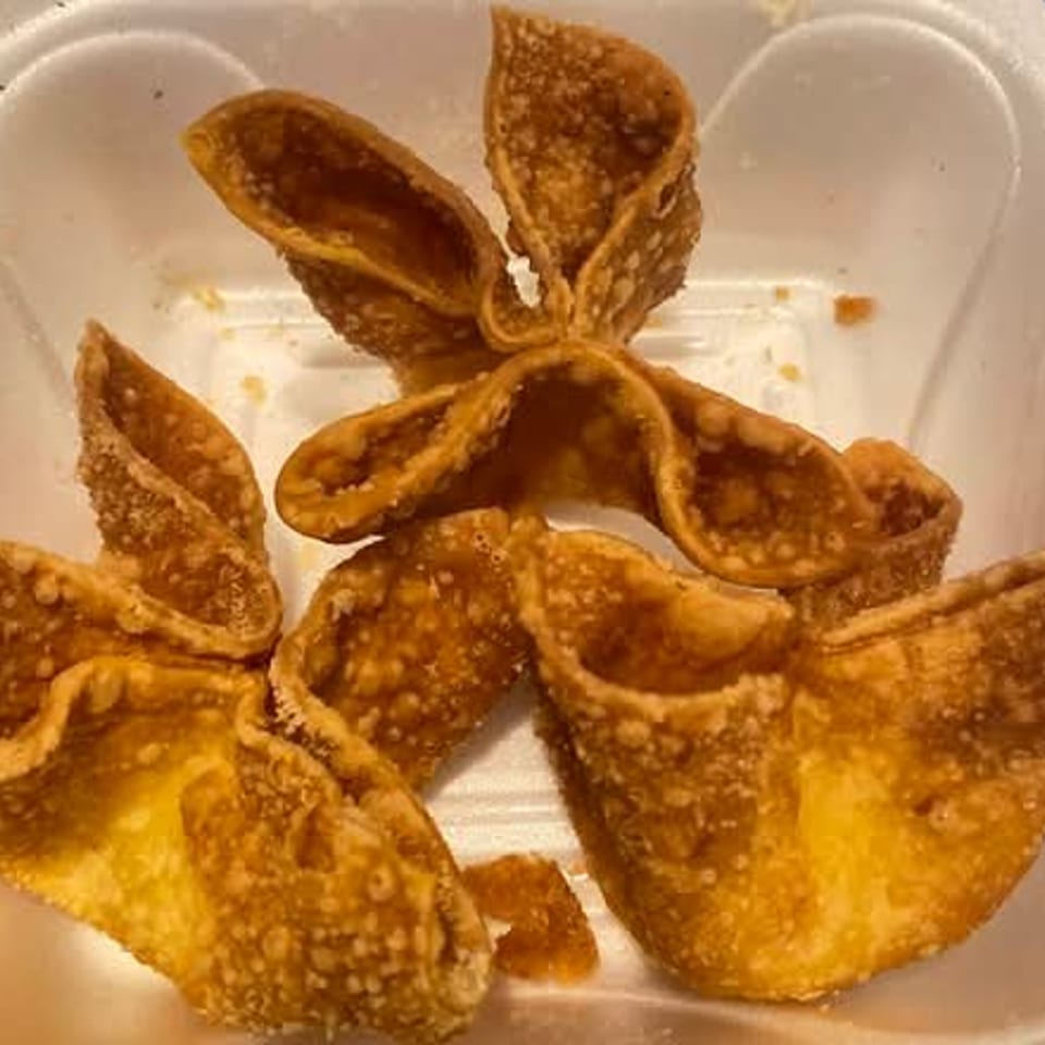 Several golden-brown, crispy crab rangoon appetizers are served in a white takeout container.