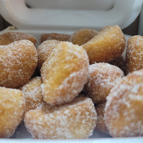 Close-up of golden-brown, sugar-dusted donut holes in a white takeout container.
