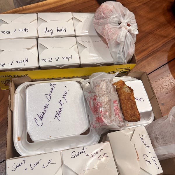 A large order of Chinese takeout food in white boxes and styrofoam containers, including "Chinese Donuts".